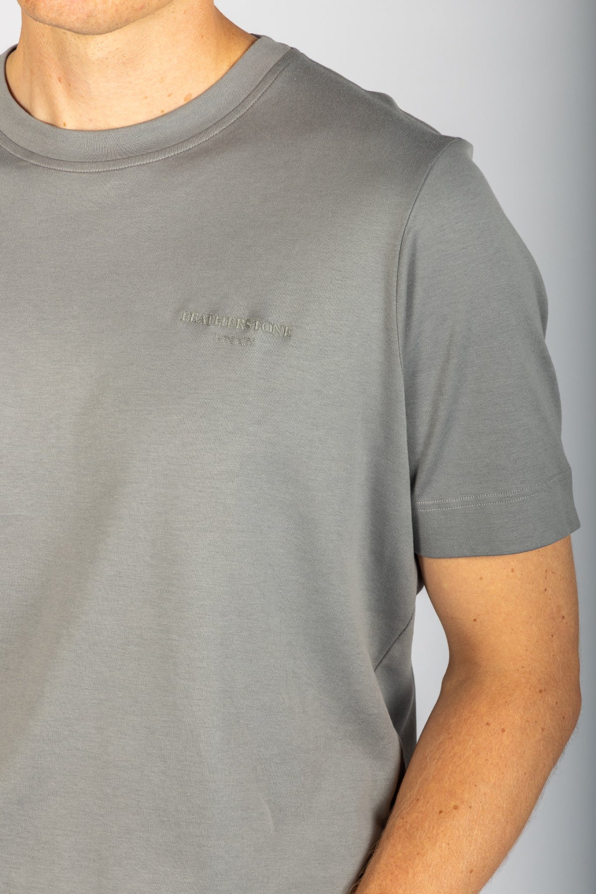 Close-up of embroidered Featherstone London logo on stone grey T-shirt