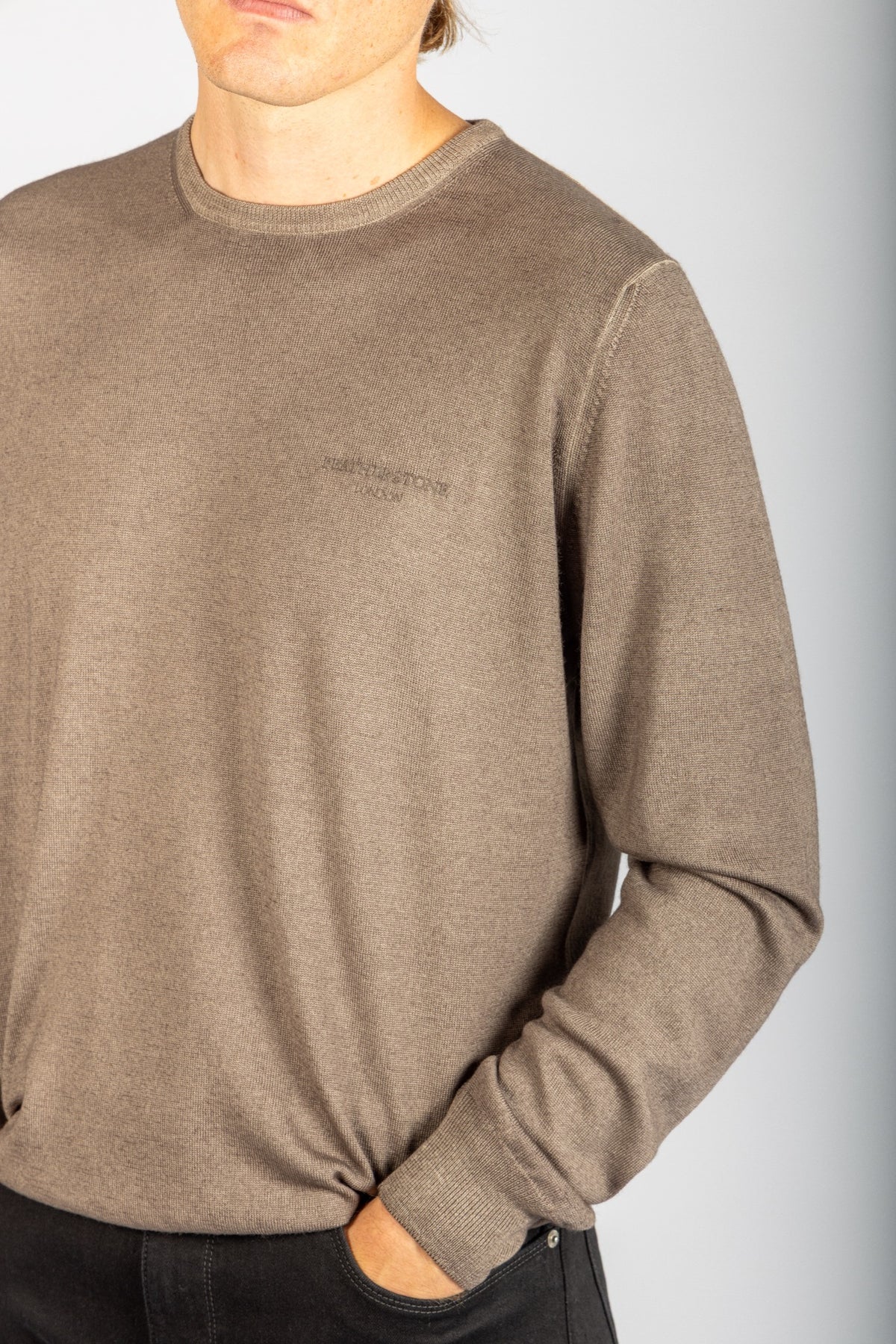 Close-up of embroidered logo and ribbed neckline on taupe wool jumper