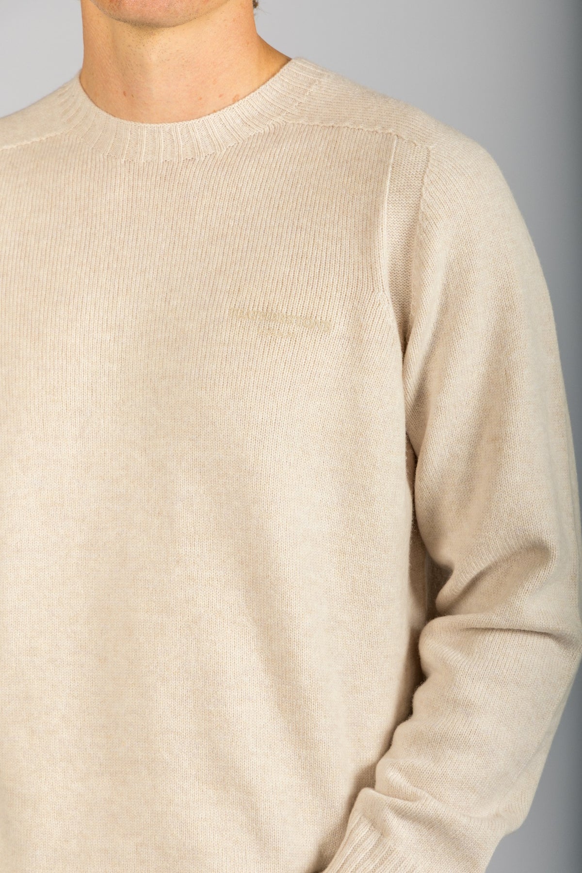Close-up of embroidered logo and marl knit texture on oatmeal wool jumper